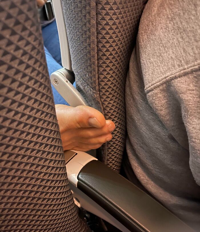 Bare foot shoved into airplane seat gap between armrest and passenger, example of next-level jerks
