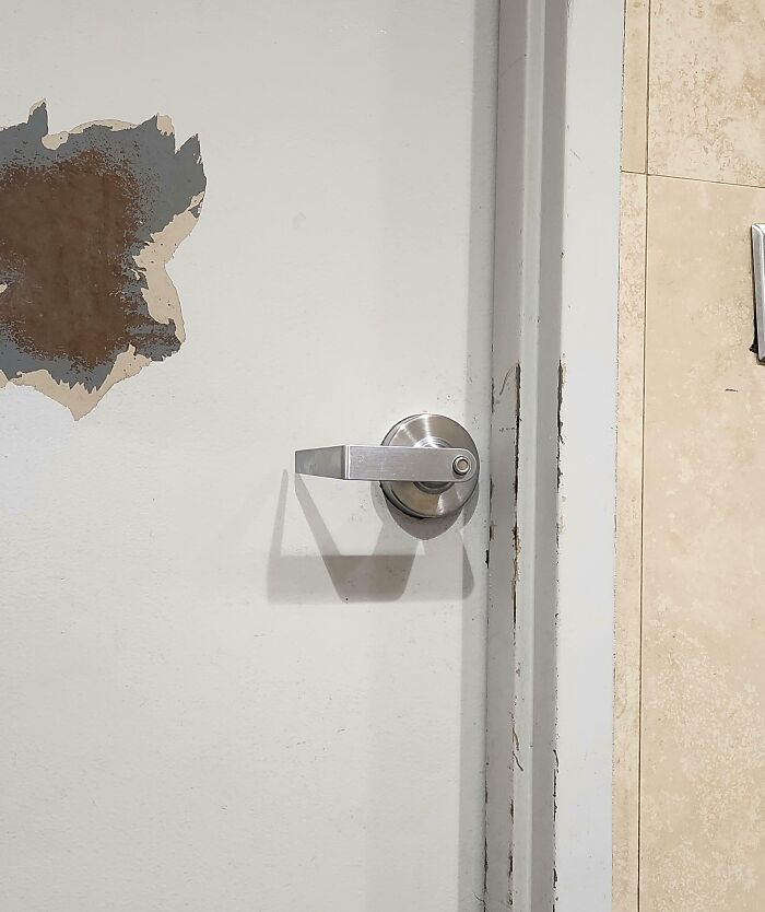 next-level jerks vandalized white door with metal lever handle, peeled paint and chipped frame near tiled wall