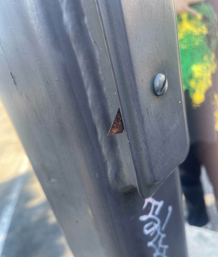 Triangular cut revealing rust in a metal street pole with graffiti, an act by next-level jerks.