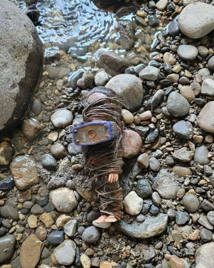 Doll wrapped in wire lying among wet rocks, evoking eerie and scary posts shared online atmosphere.