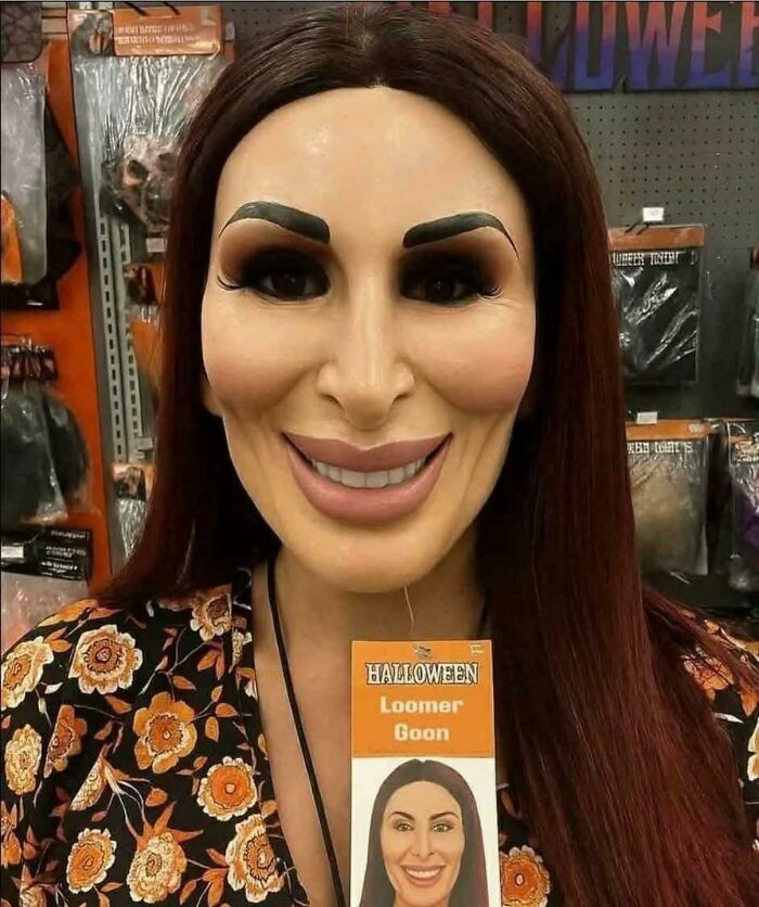 Person wearing a hyper-realistic Halloween mask with exaggerated facial features in a store with scary posts displayed.