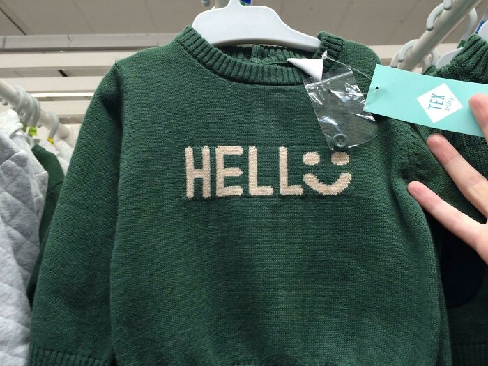 Green sweater with the text HELLO misspelled as HELLS and a smiley face, showcasing hilarious fashion fails in clothing design.