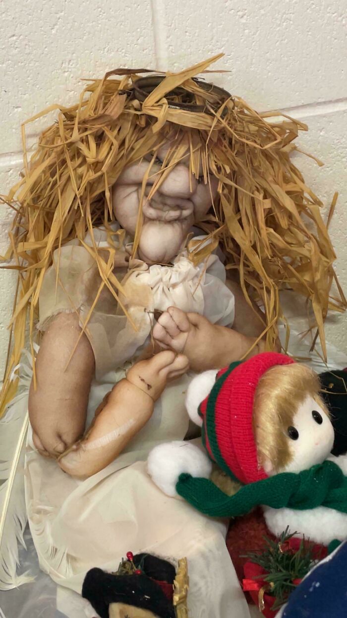 Creepy doll with straw hair and distorted face sitting against a wall, surrounded by smaller toys, scary posts online.