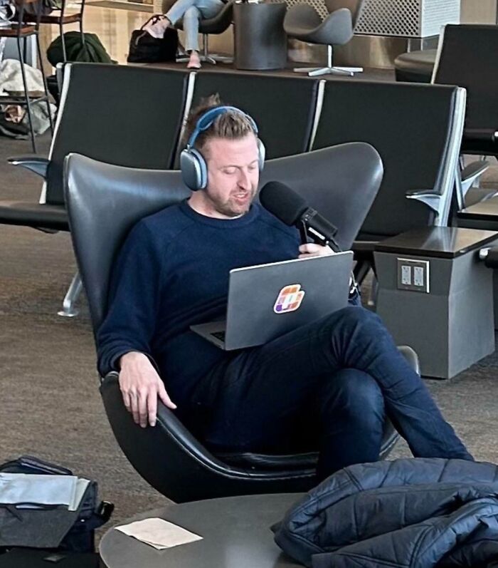 Man in airport lounge recording on laptop with headphones and handheld mic, next-level jerks