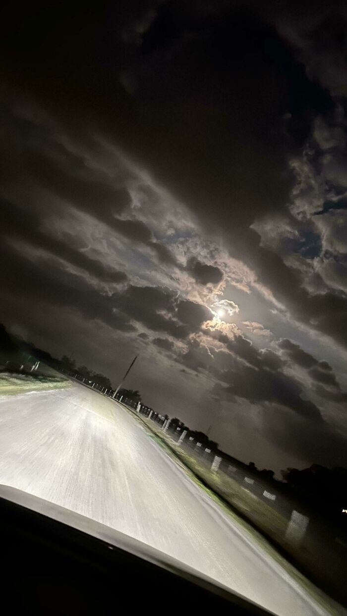 Dark night sky with dense clouds and a glowing moon over a deserted road, evoking scary posts shared online.