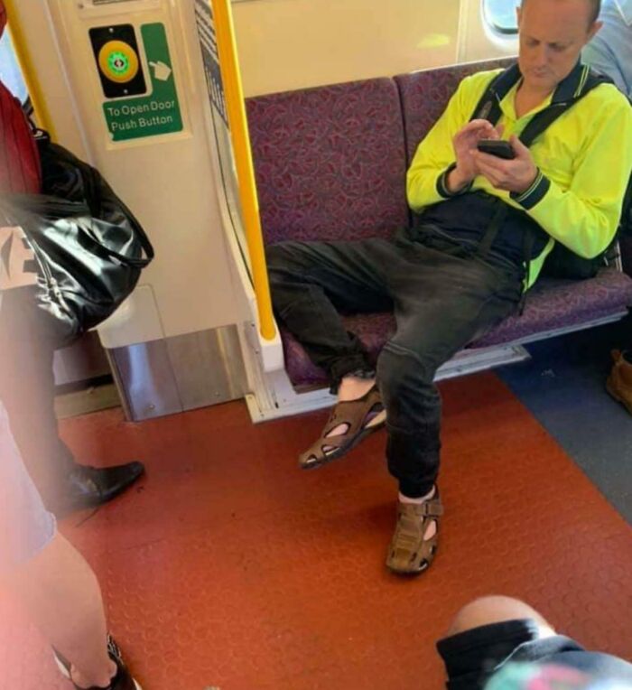 Man in hi-vis jacket sprawls across train seat with legs wide and sandals, using phone - example of next-level jerks