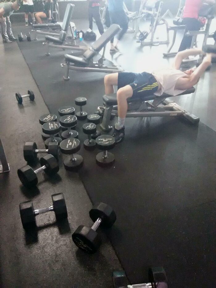 Gym bench with scattered dumbbells blocking the floor while a person lies on bench, example of next-level jerks