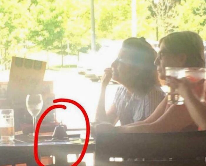 Two women at a bright restaurant table with a service bell circled, showing next-level jerks.