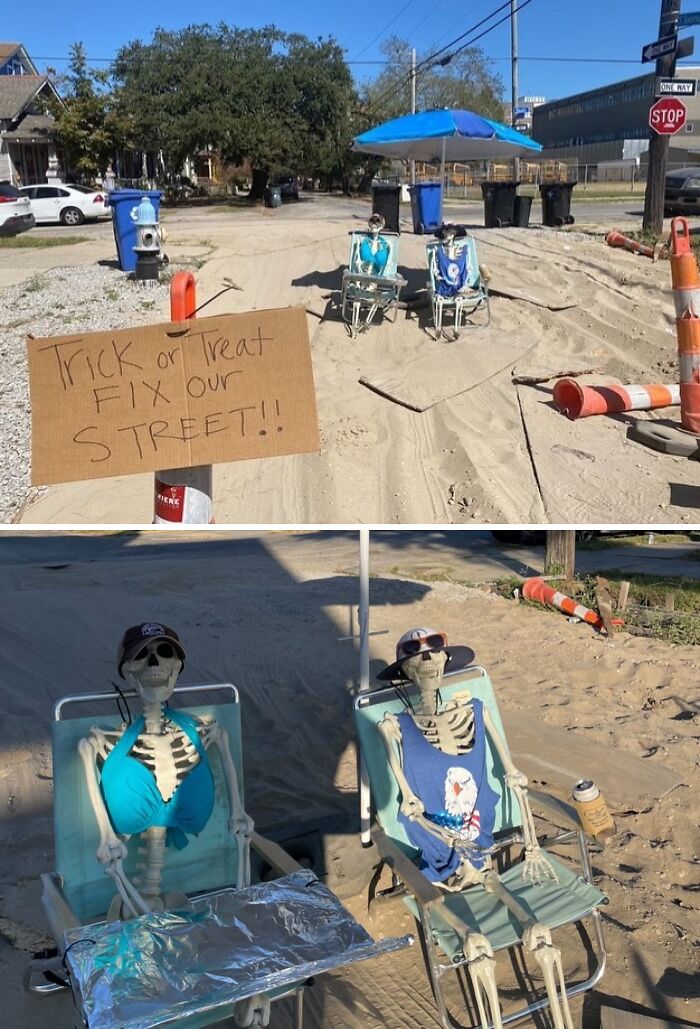 Two skeletons wearing summer clothes sitting on chairs under an umbrella on a sandy street with a fix our street sign.