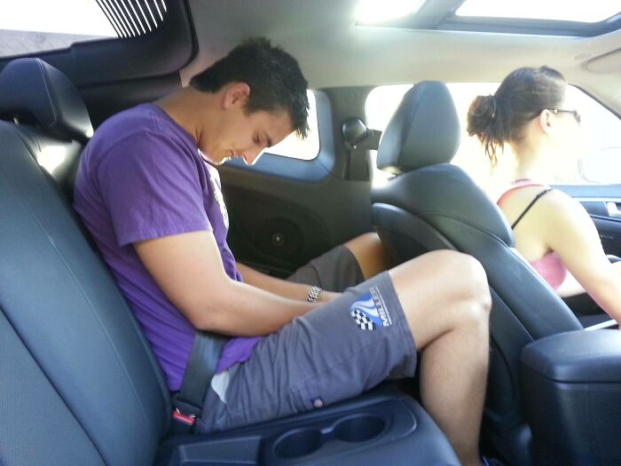 A tall person sitting uncomfortably in the backseat of a small car, struggling with limited legroom.