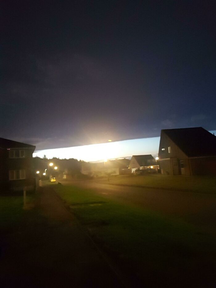 Suburban street at twilight with a straight cloud line and bright horizon, evoking glitches in the Matrix.