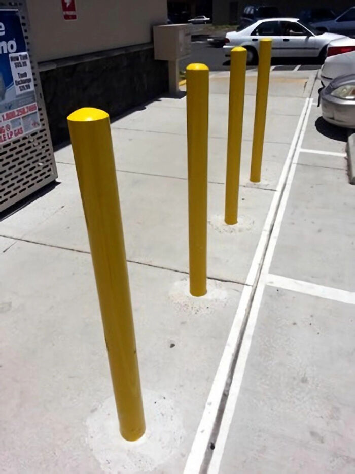 Glitches in the Matrix: four yellow bollards oddly misaligned along a parking lot