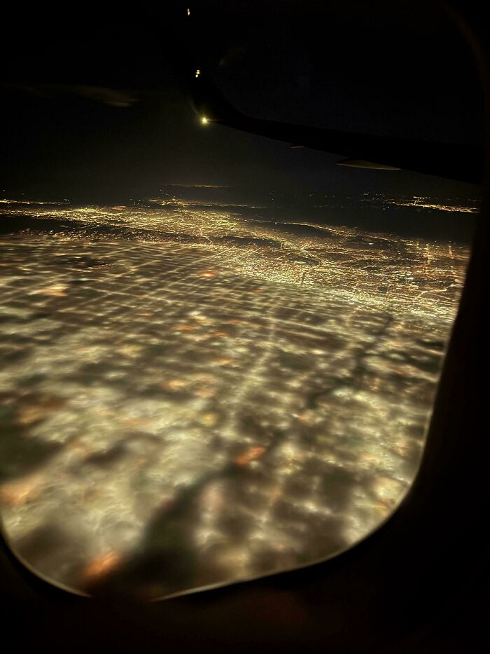 Night aerial view from airplane window showing city lights and cloud grid resembling glitches in the matrix