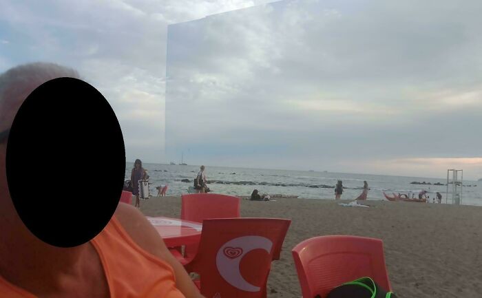 Beach scene with plastic chairs and a large reflective panel creating a mirror glitch effect, glitches in the matrix