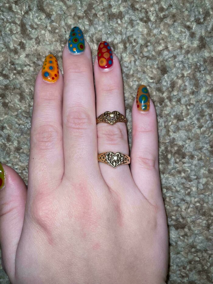 Hand with colorful dot nail art and two heart rings on beige carpet, glitches in the matrix theme