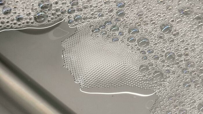 Close-up soap bubbles and water on stainless steel surface, surreal pattern evokes glitches in the matrix