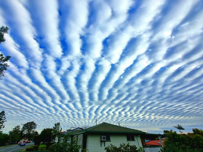Wave-like rippled clouds over a suburban house and street, evoking glitches in the matrix