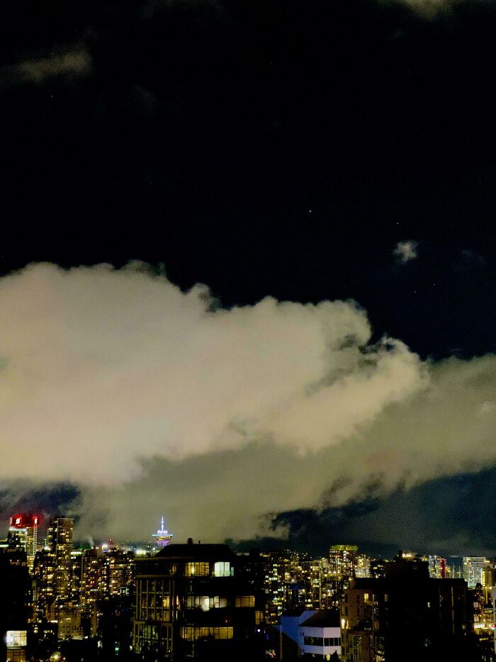 Night city skyline with glowing tower beneath a huge cloud, evoking glitches in the matrix