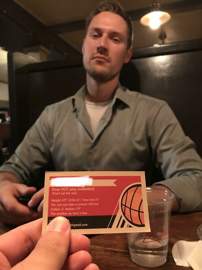 Man sitting at a table in a restaurant, holding a card that highlights struggles of tall people with height and shoe size details.