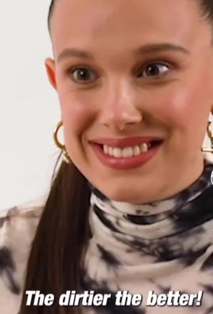 Close-up of a woman smiling widely wearing gold hoop earrings and a tie-dye top in a pop culture cringe moment.