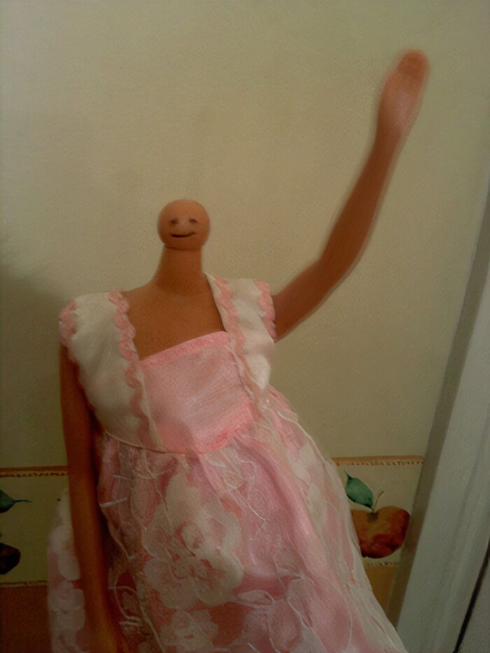 Plastic doll in a pink dress with a smiling face and raised arm, showing fun moments with siblings.