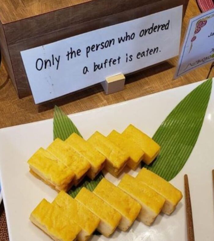 Sign with funny English translation about buffet rules next to neatly arranged yellow food pieces on a plate with chopsticks.