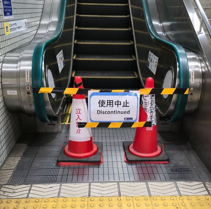 Escalator blocked with cones and sign showing funny Japan English translation error with word discontinued.