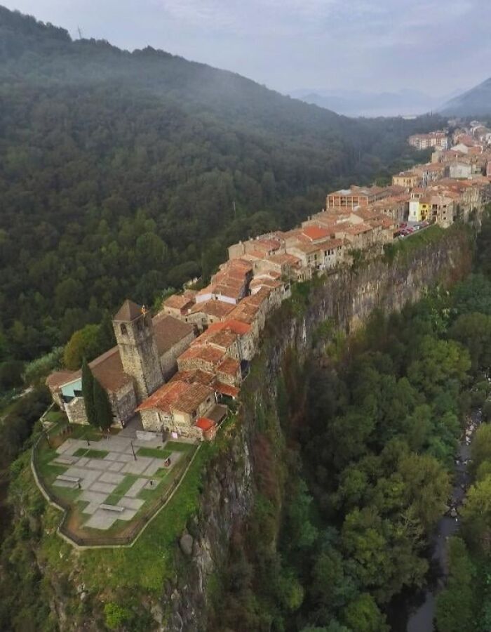 amazing photos: aerial view of a cliffside village with red-tiled roofs and church overlooking a forested valley and river
