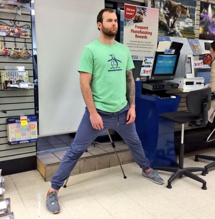 Tall man in a green shirt stretching his legs wide inside a store, illustrating common struggles only tall people face.