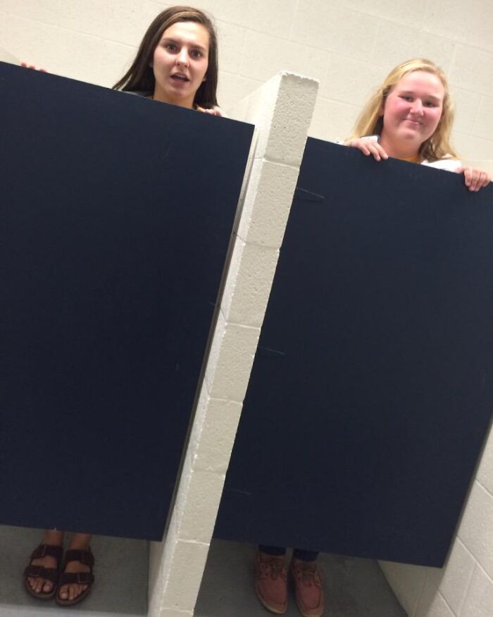 Two tall women standing in bathroom stalls with doors covering only part of their bodies, showing struggles only tall people face.