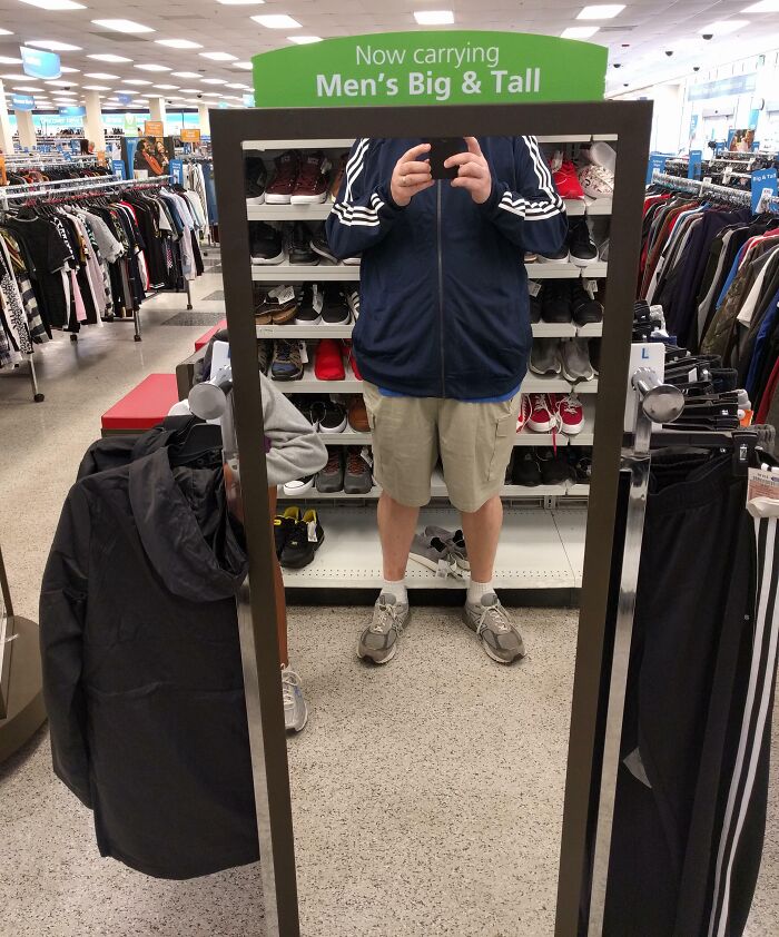Man taking a mirror selfie at a store specializing in men's big and tall clothing, highlighting tall people struggles.