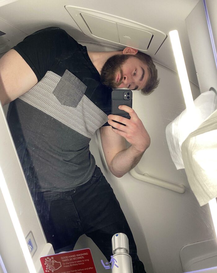 Tall man taking a selfie in an airplane bathroom showing common struggles tall people face in small spaces.