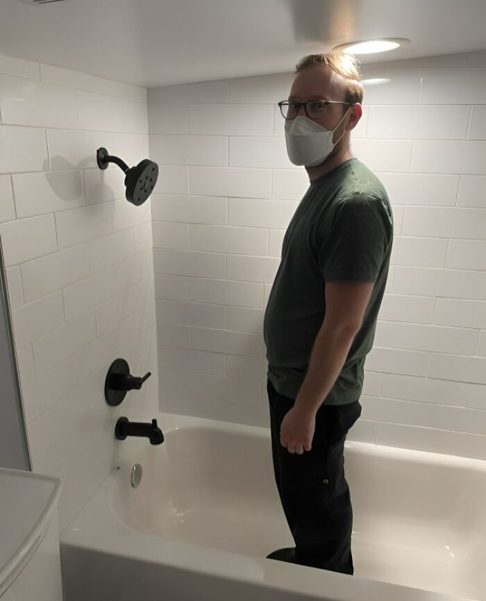 Tall person standing in a bathtub with a low ceiling, highlighting common struggles tall people face indoors.