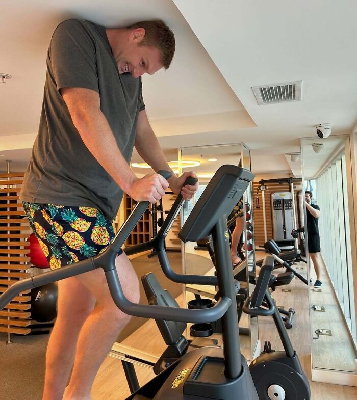 Tall man bending awkwardly on exercise machine in gym, illustrating common struggles only tall people face.