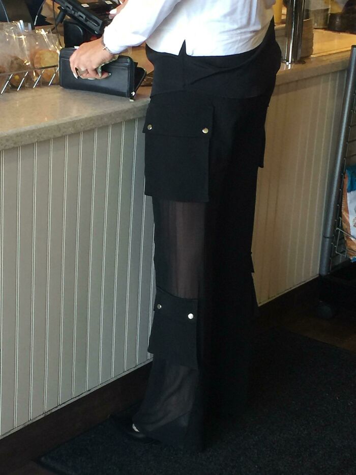 Person wearing black sheer pants with large cargo pockets standing at a counter, showcasing a hilarious fashion fail.
