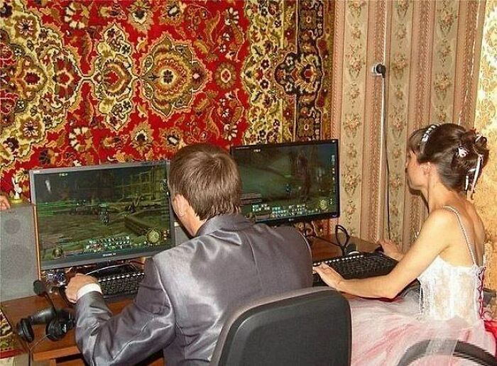 Bride and groom playing video games on dual monitors in wedding attire, an awkward wedding photo moment.