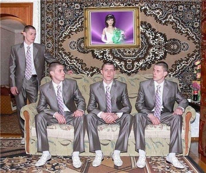Four identical men in matching silver suits and white sneakers sitting and standing in a living room awkward wedding photo.
