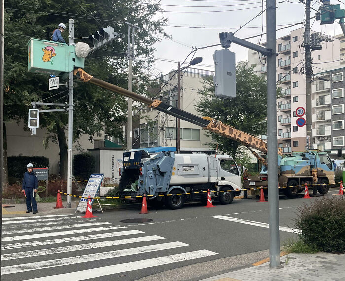 Utility workers using a giraffe-patterned cherry picker to maintain traffic lights, showcasing impressive country implementations.