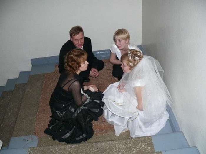 Four people including a bride in a wedding dress sitting awkwardly on stairs in an awkward wedding photo moment.