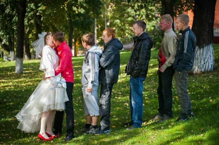 Bridal couple kissing as a group of awkward groomsmen stand in line outdoors in a funny wedding photo moment.