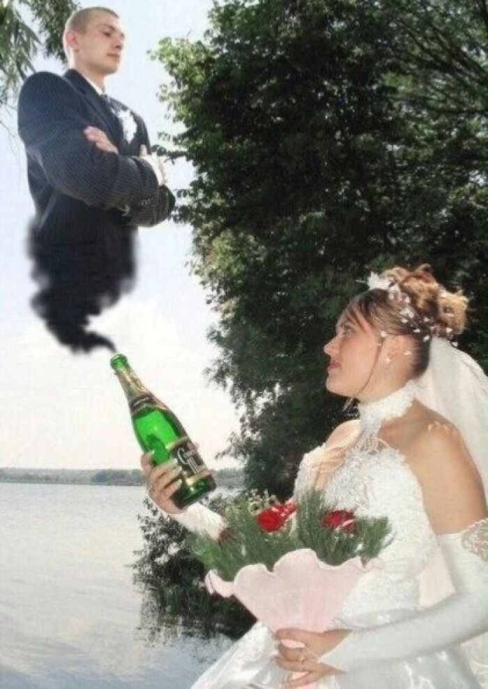 Bride holding a champagne bottle with smoke forming a groom’s upper body in an awkward wedding photo by the water.