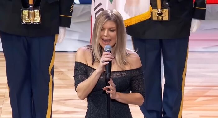 Woman singing the national anthem on court with guards standing behind, one of the pop culture moments that made people cringe hard