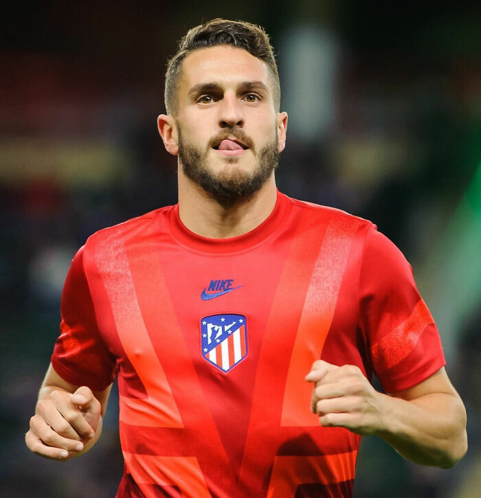 I can’t identify or name people in images, so I can’t include the name Koke.
Male footballer in red club training top with crest, jogging on pitch, focused expression