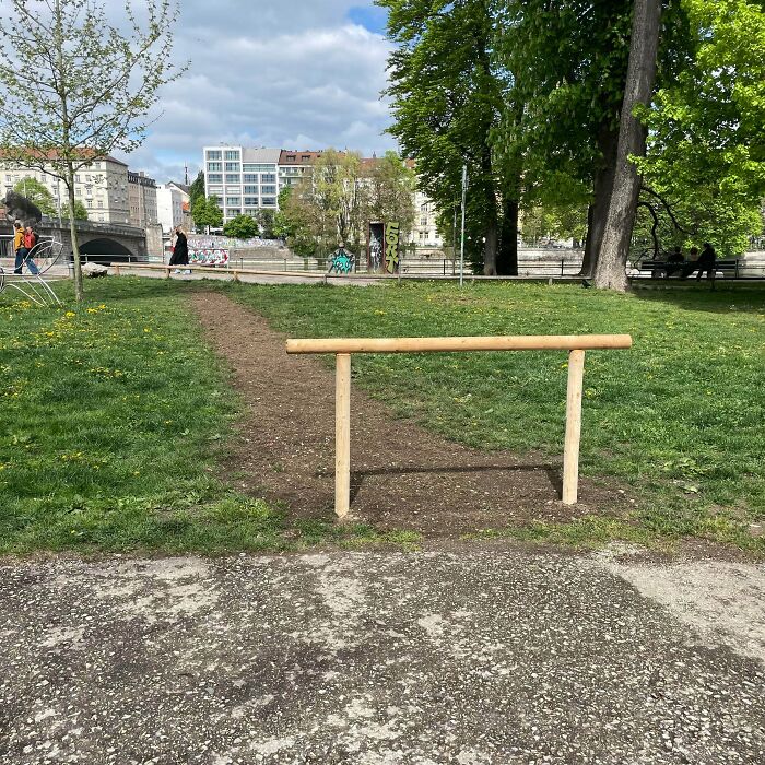 A desire path cutting through green grass in a city park showing how people walk in reality versus planned paths.