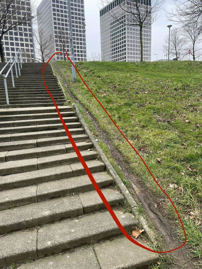 Desire path worn on grassy slope beside city stairs showing how people walk versus planned routes in urban areas.