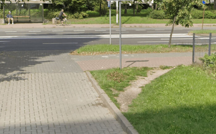 Desire path cutting through grass beside paved sidewalk showing how people walk differently from city planning design.
