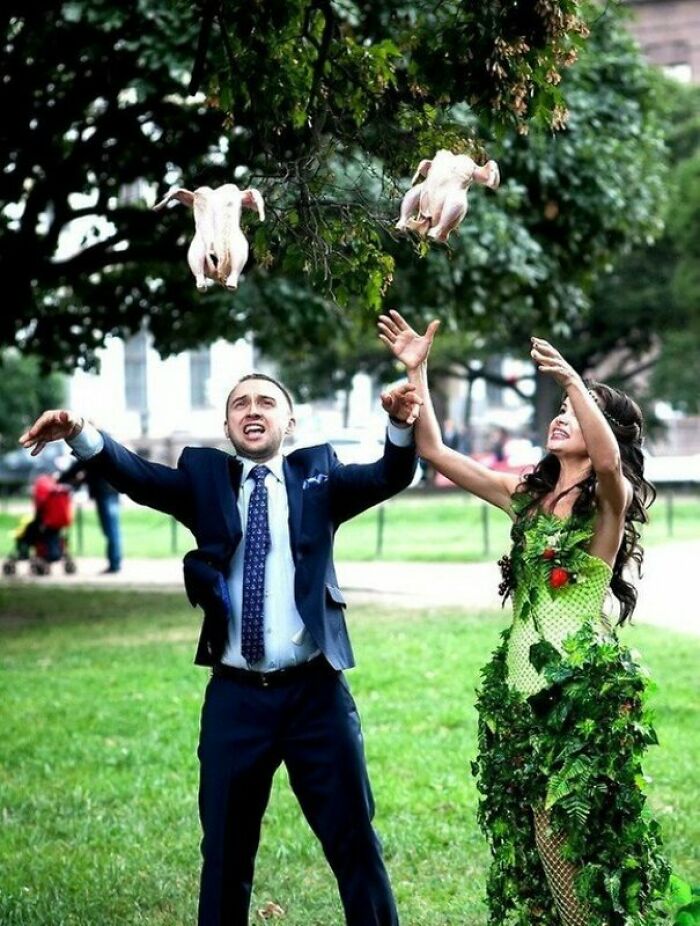 Pareja de novios lanzando pollos crudos al aire en un parque, foto de boda divertida y equivocada con toque legendario.