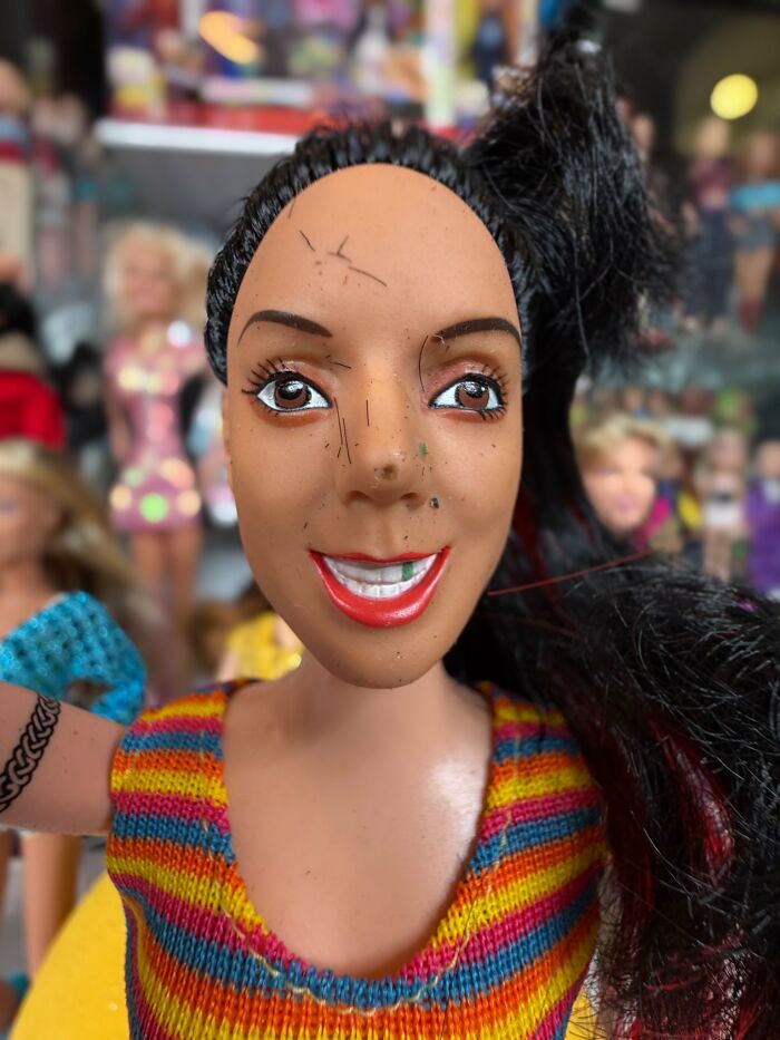 Offensively ugly celebrity doll with a damaged face and colorful striped top among other dolls in the background