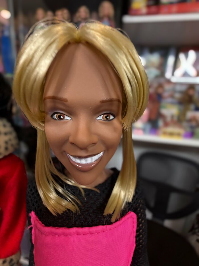 Close-up of an offensively ugly celebrity doll with blonde hair and exaggerated facial features in a pink outfit.