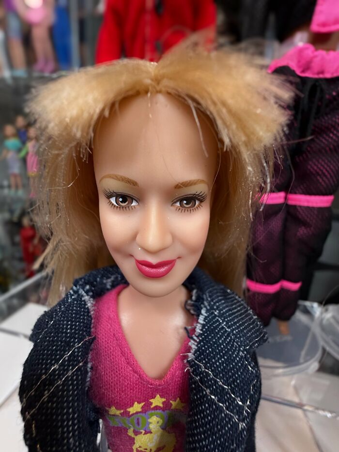 A close-up of an offensively ugly celebrity doll with messy hair, exaggerated makeup, and a denim jacket.